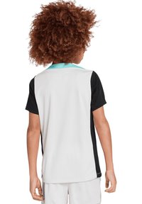 Maglia atletica per ragazzi con corpo in rete bianca, maniche nere e colletto turchese. Presenta una vestibilità comoda e un design sportivo.