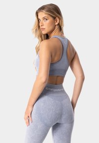 Gaiši zilas sporta krūšturis un legingi ar ribotām akcentēm, ar bezšuvju dizainu un maigām tekstūrām. Logo redzams uz jostas.