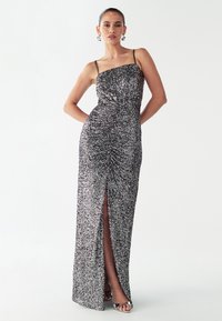 Zwart-zilveren pailletten jurk met een aansluitend silhouet, spaghettibandjes en een hoge split tot aan de dij. Soepele textuur en geplooide details.