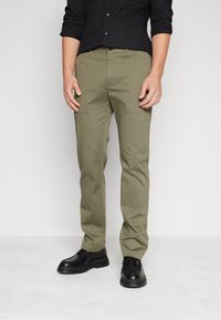 Pantaloni khaki in misto cotone, con un design slim fit, parte frontale piatta, passanti per cintura e tasche laterali, abbinati a scarpe nere.