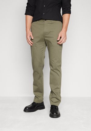 Pantaloni khaki in misto cotone, con un design slim fit, parte frontale piatta, passanti per cintura e tasche laterali, abbinati a scarpe nere.