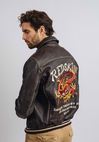 Veste en cuir marron de type bombardier avec un grand motif de dragon brodé dans le dos, et des poignets et une taille en tricot.