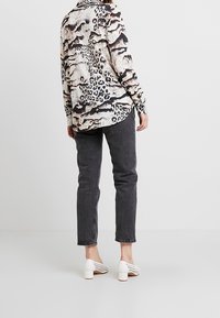 Hemdenhemd mit beige-schwarzem Tiermuster, kombiniert mit dunkelgrauen Jeans und weißen, perforierten Pumps.