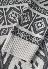 Pull en maille présentant un motif géométrique en noir et gris, avec des poignets côtelés et une texture douce. Le design comprend des hexagones et des diamants.