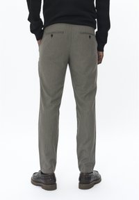 Grijze, gestructureerde pantalon met een subtiele houndstooth-patroon; heeft twee achterzakken met druksluitingen. Draagt met donkere schoenen.