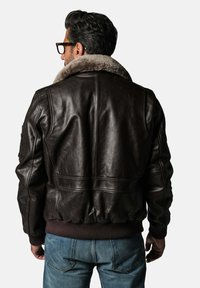 Veste aviateur en cuir marron avec un col en fausse fourrure, des poignets et un ourlet côtelés, présentant une finition lisse et un design minimaliste.