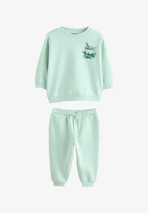 Mintgrønt sæt til småbørn med sweatshirt og bukser med ribstrikkede manchetter, der har en grafik af en smilende chokolademælkekarton på brystet af sweatshirten.