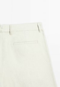 Pantalons beiges à coupe droite, fabriqués en tissu texturé, avec une petite poche arrière et des passants de ceinture.