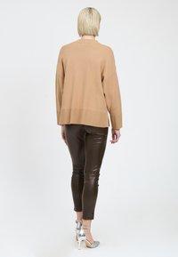 Pullover beige oversize con spalle scese, orlo a coste e spacchi laterali, abbinato a pantaloni in pelle marrone aderenti e scarpe con tacco alto argentate.