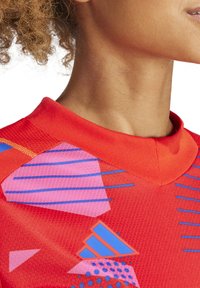 Rode sportshirt van textuurstof, met blauwe en roze geometrische patronen en een ronde kraag.