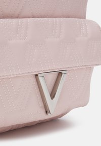 Rosa quiltad handväska med ett upphöjt sicksackmönster, silvermetallaccent i form av ett "V" och slät yta.