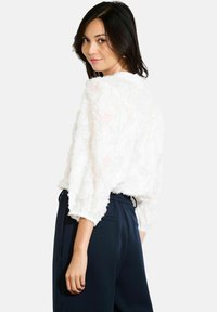Blusa bianca in pizzo floreale con maniche ampie a tre quarti, abbinata a pantaloni navy a vita alta con elastico in vita e due tasche.