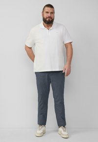 Witte poloshirt, donkere geruite broek en beige sneakers. De poloshirt heeft een kraag; de broek is taps toe en heeft een subtiel patroon.
