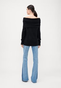 Schwarzer schulterfreier Pullover mit geripptem Muster. Kombiniert mit hellblauen Schlagjeans, die seitlich ein dunkelblaues Panel aufweisen.