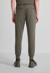 Joggers verde oliva hechos de una tela suave con cintura elástica, piernas ajustadas y dos bolsillos traseros, combinados con zapatillas oscuras.