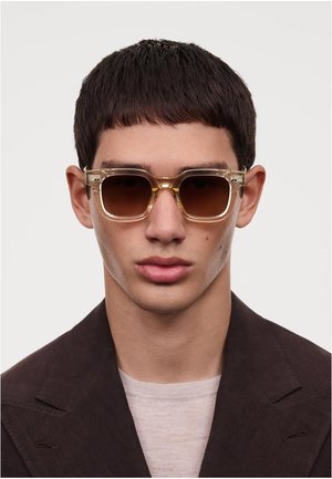 Lunettes de soleil à monture carrée en acétate transparent teinté en jaune et avec des verres marron, dotées d'accents métalliques près des charnières.