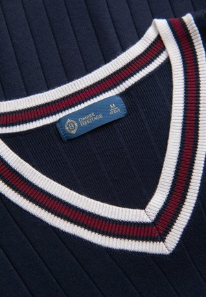 Marineblauer, gerippter Pullover mit V-Ausschnitt, der mit weißen, roten und marineblauen Streifen verziert ist, und einem Ombre Heritage Etikett in Größe M am Kragen innen.