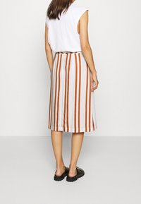 Jupe midi rayée avec des rayures verticales orange et blanches, fabriquée en tissu léger. Associée à un haut sans manches blanc ample et des chaussures noires.