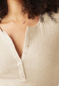 Top beige acanalado con escote en V y cinco botones en la parte frontal. La tela tiene un acabado texturizado que añade interés visual.