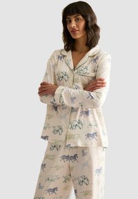 Conjunto de pijama con estampado de animales en tela suave, presentando un fondo beige con dibujos de animales en azul y verde, con ribetes en contraste y una camisa con botones.