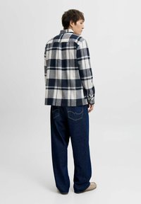 Camisa de cuadros en azul marino, blanco y gris con mangas largas y corte recto; combinada con unos jeans de corte ancho en azul oscuro y zapatos de color claro.