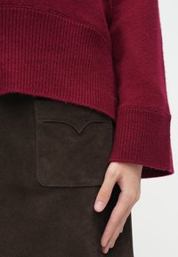 Burgundská pletená svetr s žebrovaným lemem, v kombinaci s tmavě hnědou semišovou sukní s kapsou a zaobleným švem.