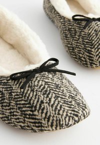 Black and cream patterned slippers with a soft, fluffy lining and black ribbon accents on the front, featuring a rounded toe design.