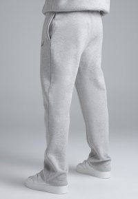 Grijze joggingbroek gemaakt van zachte stof, met een tailleband met trekkoord, zijzakken en taps toelopende pijpen. Gecombineerd met witte sneakers.