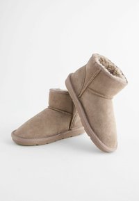 Tanfarbene Wildlederschuhe mit weichem Futter aus Fell, runder Zehenpartie und genähten Akzenten. Die Sohle ist flach und strukturiert für besseren Grip.