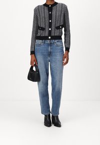 Texturerad svart och vit Stickad cardigan med stora knappar, två framfickor, ihop med ljusblå jeans och svarta klackiga ankelboots.