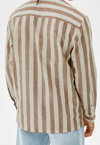 Lätt, randig skjorta i brunt och kräm. Har långa ärmar, knäppta manschetter och en rundad nederkant. Tillverkad av ett texturerat tyg.