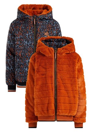 Personne portant une veste zippée en peluche orange avec doublure imprimé léopard, un haut noir, un jean bleu clair à jambes larges et des bottes bleues à lacets.
