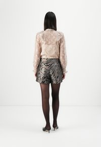 Genomskinlig beige blus med prickar, kombinerad med shorts med metallisk zebramönster. Svarta ogenomskinliga strumpbyxor och svarta klackar fulländar looken.