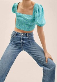 Blaues florales Cropped-Top mit Puffärmeln, kombiniert mit hoch geschnittenen hellblauen Jeans. Das Top hat einen quadratischen Ausschnitt und einen strukturierten Stoff.