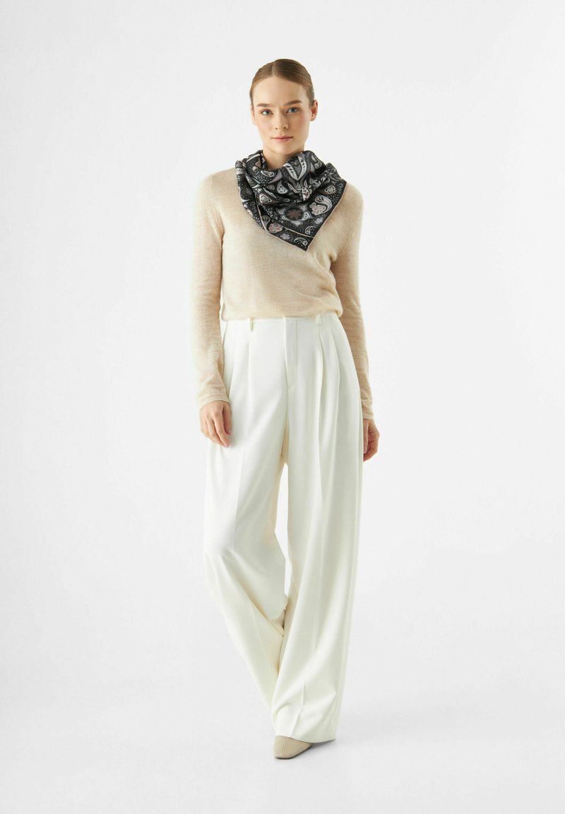 Lichtbeige trui, hooggetailleerde witte broek, zwart dessin sjaal geknoopt in een driehoekvorm, schoenen in neutrale tinten. Eenvoudig, elegant ontwerp.