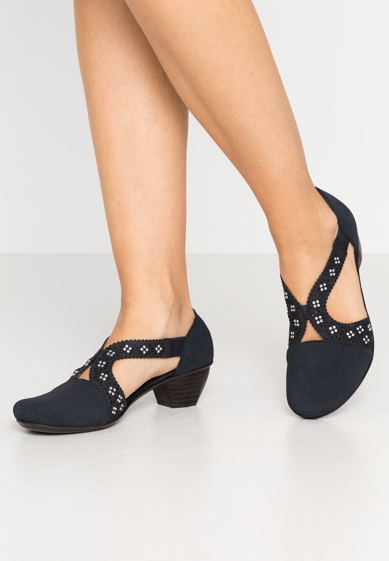 Chaussures bleu marine à petit talon, avec des motifs floraux découpés et des surpiqûres décoratives sur les brides. Matière douce semblable au daim.