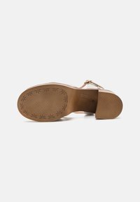 Sandal con tacco alto beige con tomaia in pelle liscia, cinturino alla caviglia e suola in gomma testurizzata con motivo floreale.