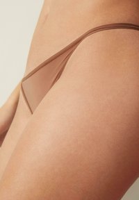 Brauner transparenter Tanga mit einem minimalistischen Design. Weiche, glatte Textur und dünne Träger, die eine sleeke Silhouette betonen.