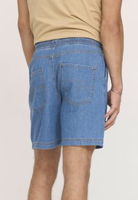 Shorts en denim de couleur bleue, avec une taille élastique, deux poches arrière avec des coutures décoratives et une coupe décontractée.