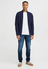 Námornícky zipsový kardigán, textúrovaná tkanina, biela tričko, tmavomodré džínsy a šedé tenisky s bielymi prúžkami. Jednoduchý a priliehavý dizajn.