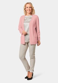 Helles rosa Cardigan mit langen Ärmeln und Taschen, getragen über einem grauen Oberteil; kombiniert mit beigen hochgekrempelten Hosen und schwarzen High Heels.