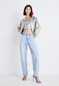 Silver metallic cropped jacket, light blue relaxed-fit jeans, and silver strappy heels. Smooth textures with a shiny finish and button details.