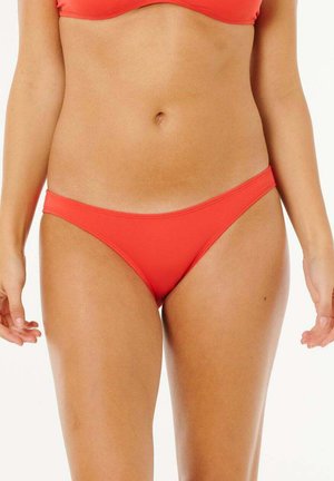 Femme portant un bas de bikini rouge uni et un haut assorti, cadrée à mi-torse avec les bras détendus sur les côtés, sur fond blanc.