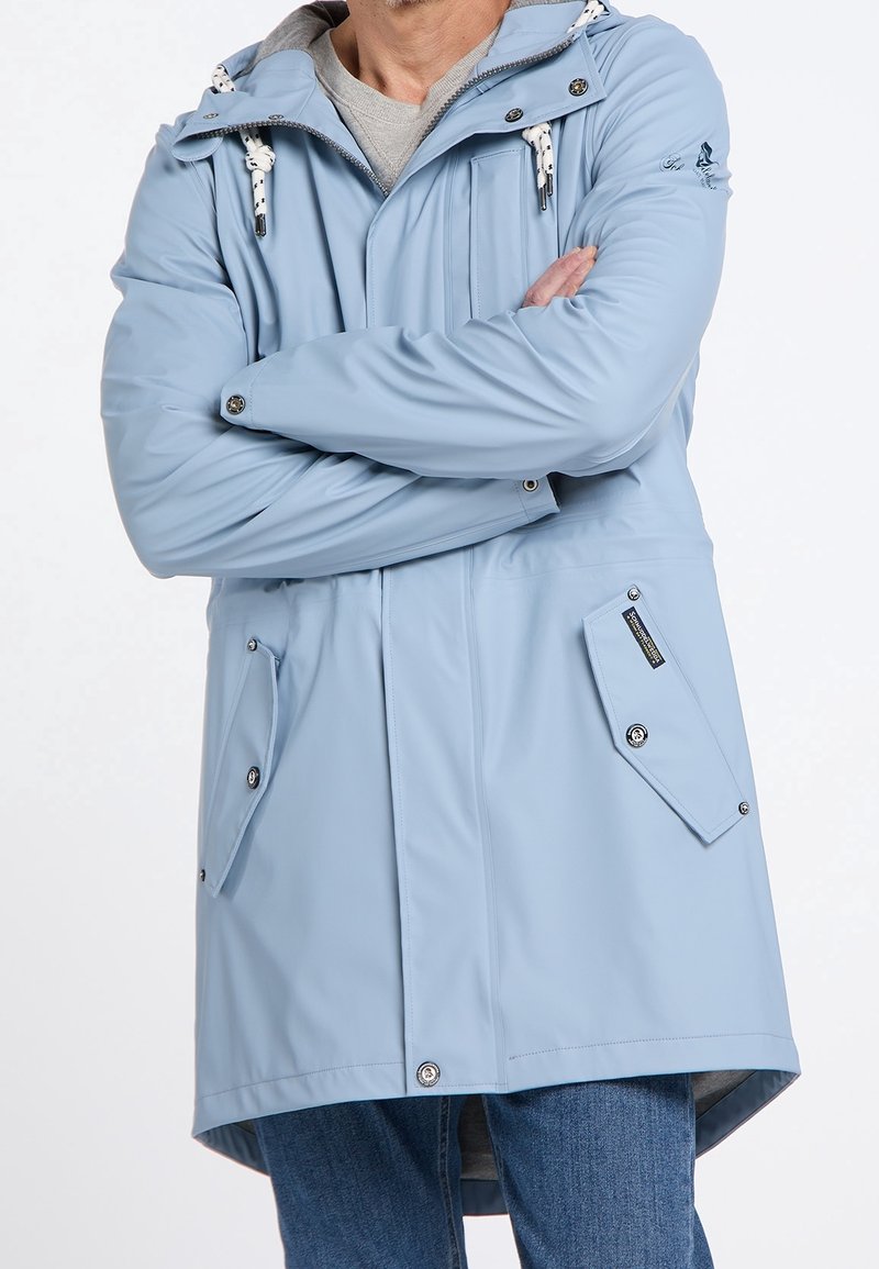 Vaaleansininen vedenpitävä parka, jossa on huppu, vetoketjukiinnitys, napit ja useita sivutaskuja. Ominaisuuksiin kuuluu sileä pinta ja säädettävät nyörit.