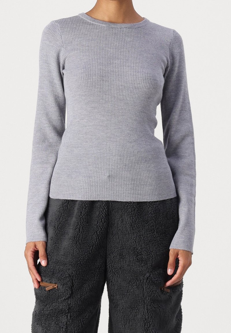 Personne portant un haut ajusté à manches longues côtelé gris clair et un pantalon en polaire noire texturée avec poches avant zippées.