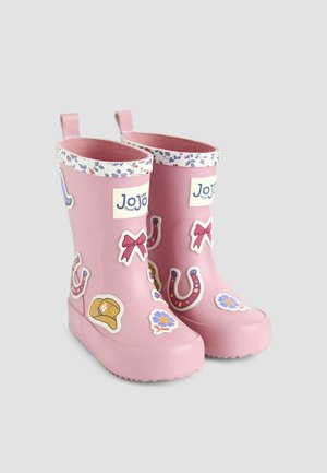 Rosa Gummistiefel mit Blumenrand, die mit verschiedenen bunten Aufklebern, darunter Schleifen, Hufeisen und Blumen, verziert sind.