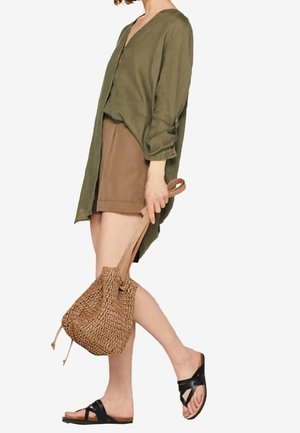 Blusa de lino verde oliva, pantalones cortos marrones, sandalias negras, sosteniendo una bolsa tejida color cuero claro. Corte suelto, escote en v, pantalones cortos a la altura de la rodilla, estilo minimalista.