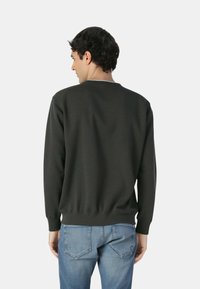 Felpa grigio scuro con polsini e scollatura a costine, realizzata in tessuto morbido. Abbinata a jeans blu, con taglio e vestibilità rilassati.