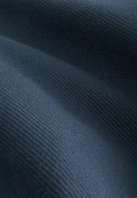 Tmavomodrý materiál s textúrovaným, ryhovaným vzorom. Tkanina sa javí ako jemná a hladká s miernym leskom a rôznymi hĺbkami.