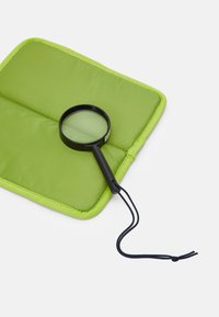Svart förstoringsglas på en ljusgrön vadderad matta med kontrasterande sömnad, utrustad med ett svart snöre för enkel hantering.